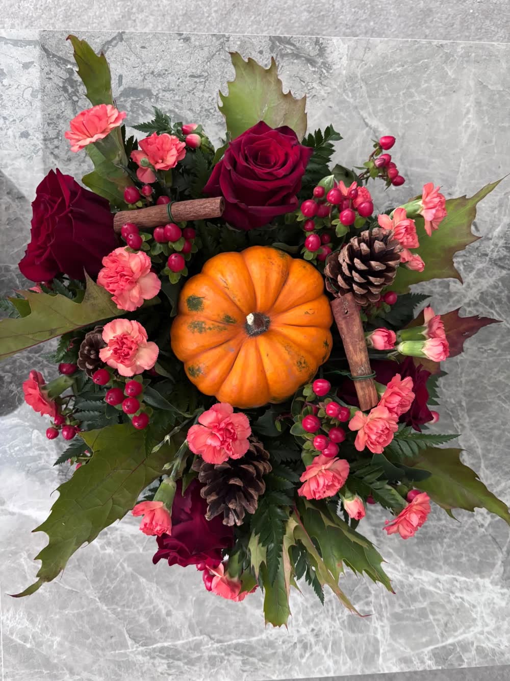 Autumn table arrangement with red roses, pink carnations, pine cones and a pumpkin