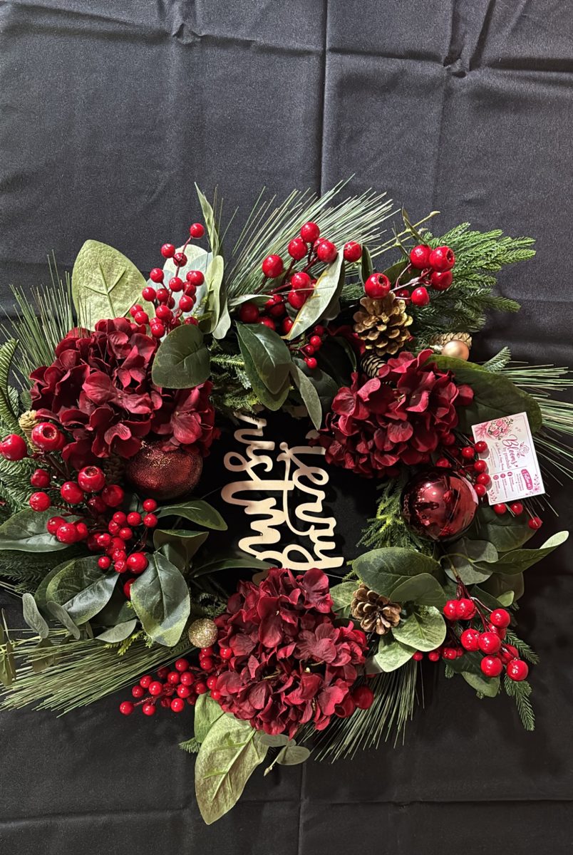 Wreath of deep red hydrangeas, red berries and pine around a wooden Merry Christmas sign