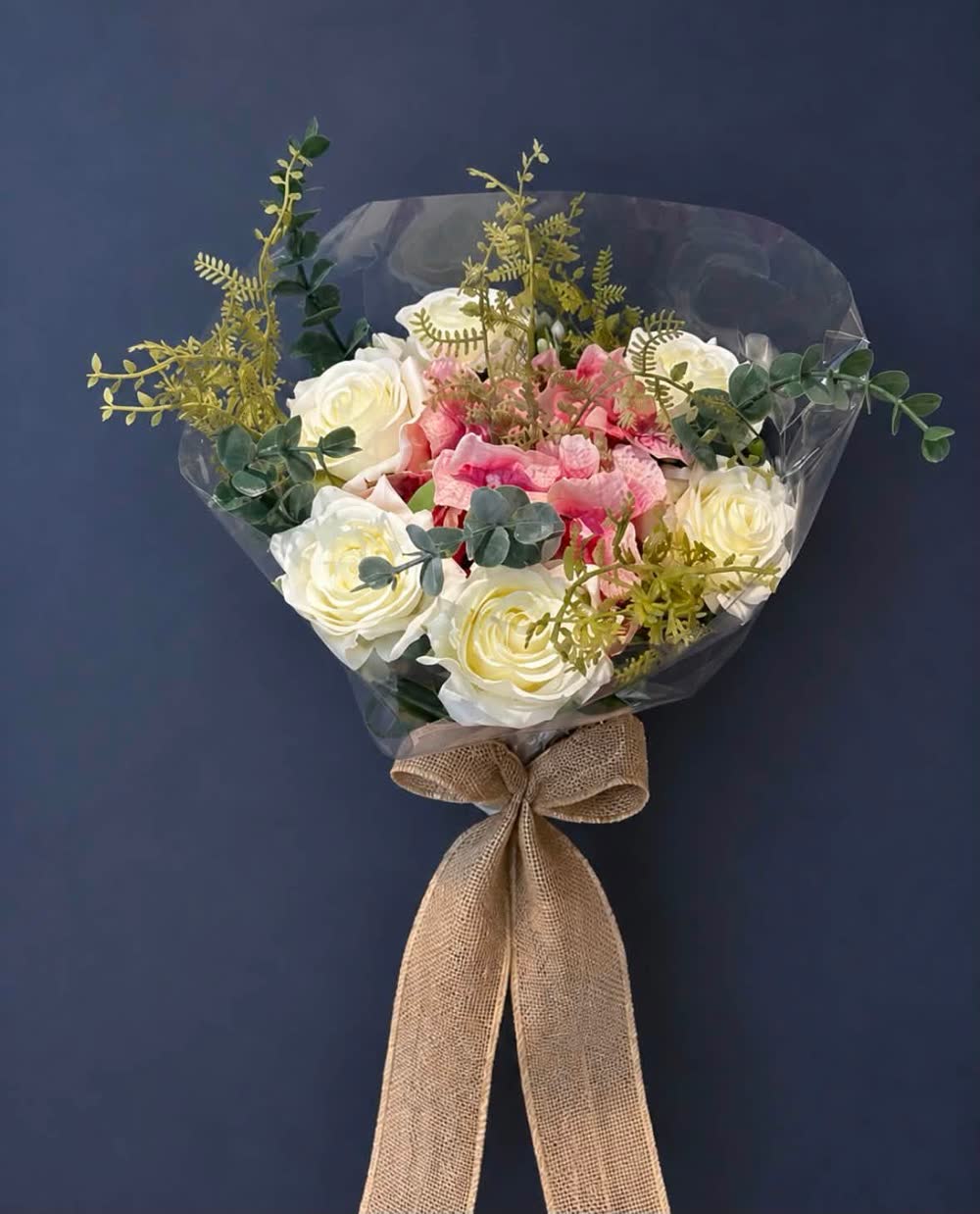 Wrapped bouquet of cream and pink roses tied with a hessian bow